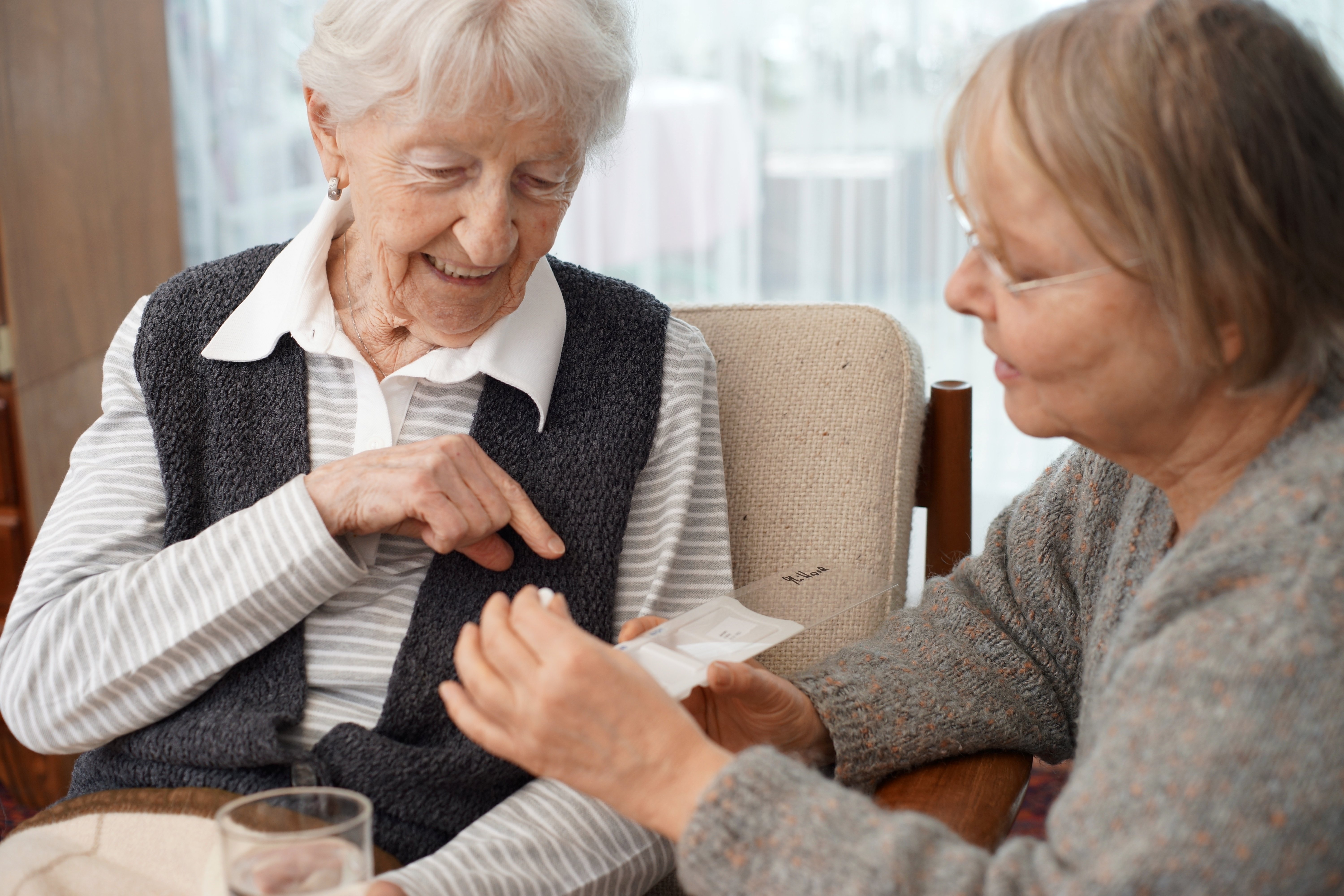 older-woman-sitting-and-pointing-to-medication-with-her-daughter