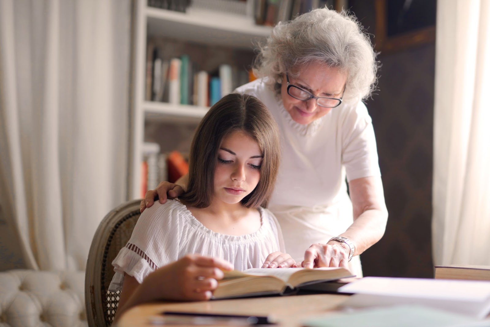 Young girl reading book with senior woman helping her