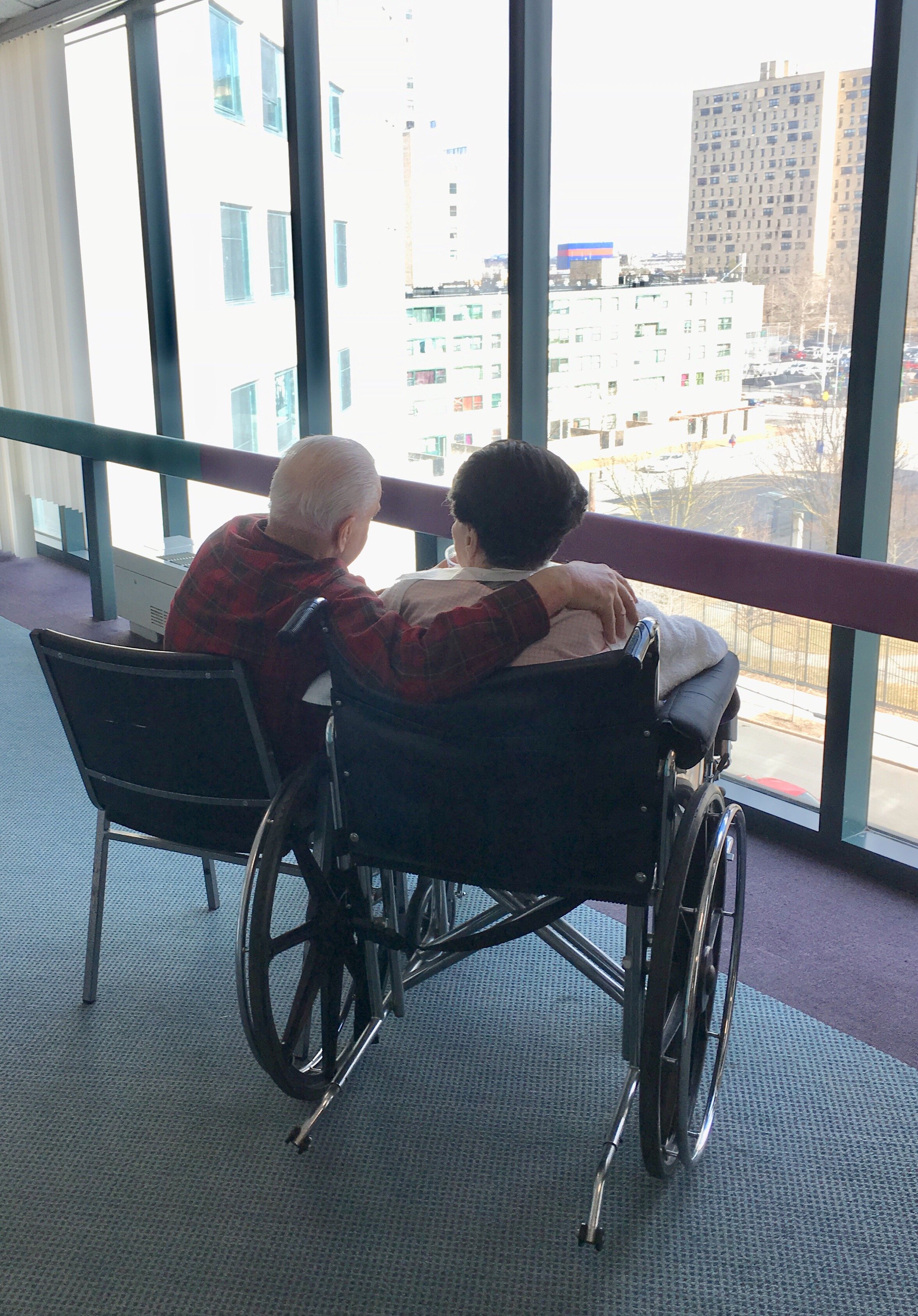 two-elder-people-in-wheelchairs-embracing-with-city-view