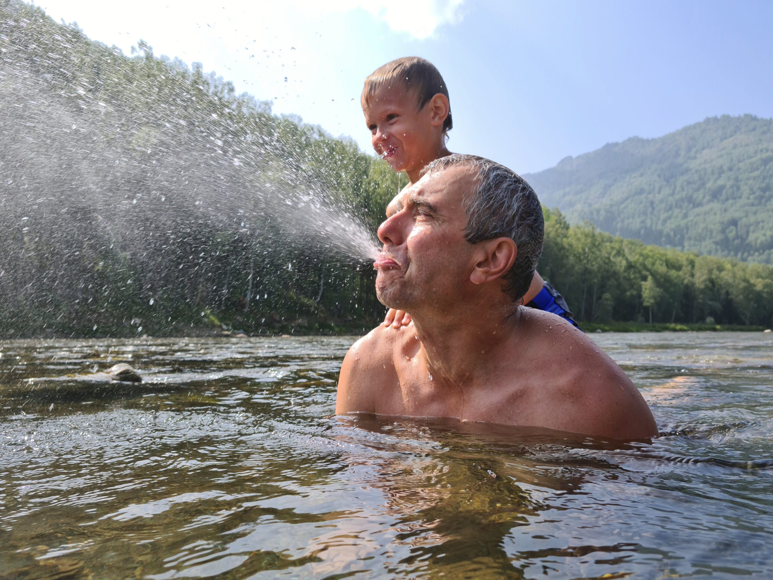 senior-man-playing-in-river-with-grandson