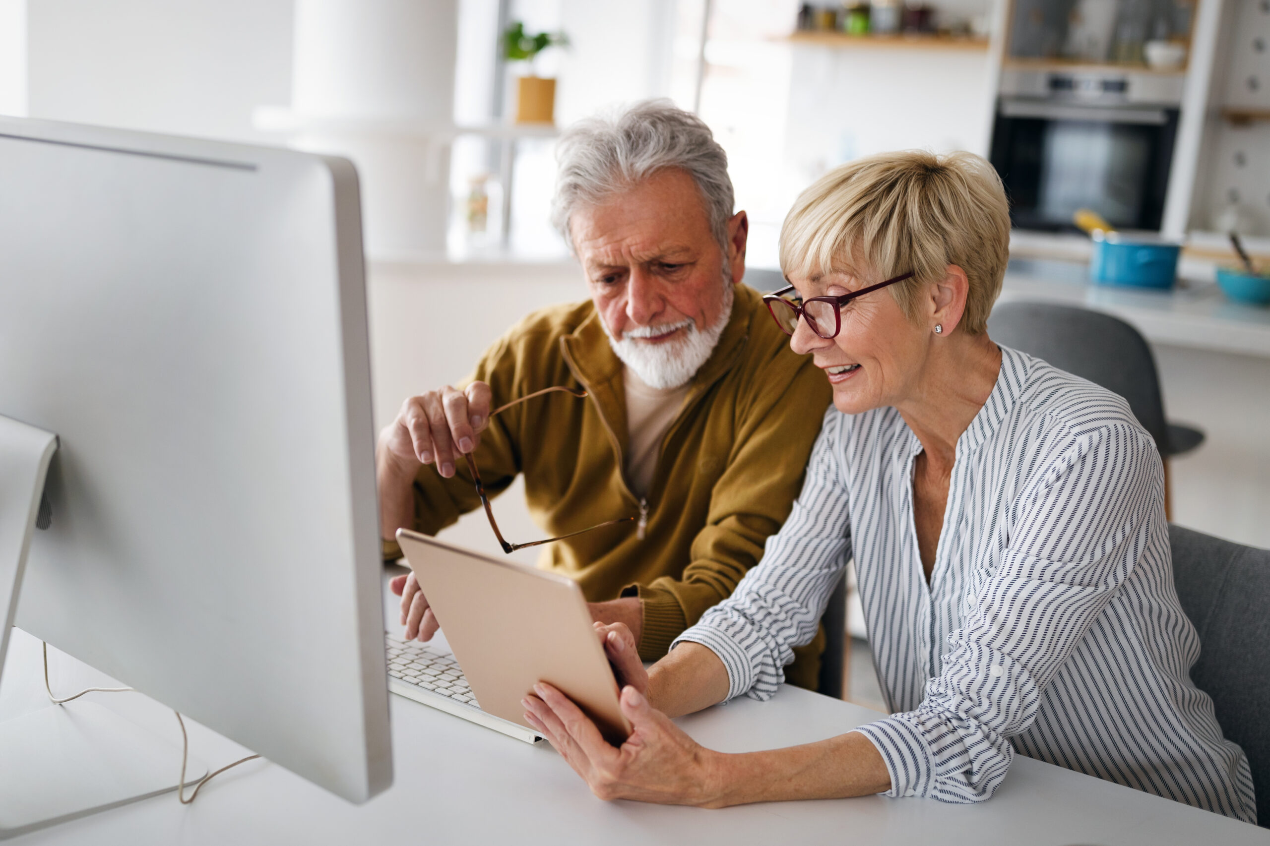 senior-couple-looking-at-ipad-and-desktop