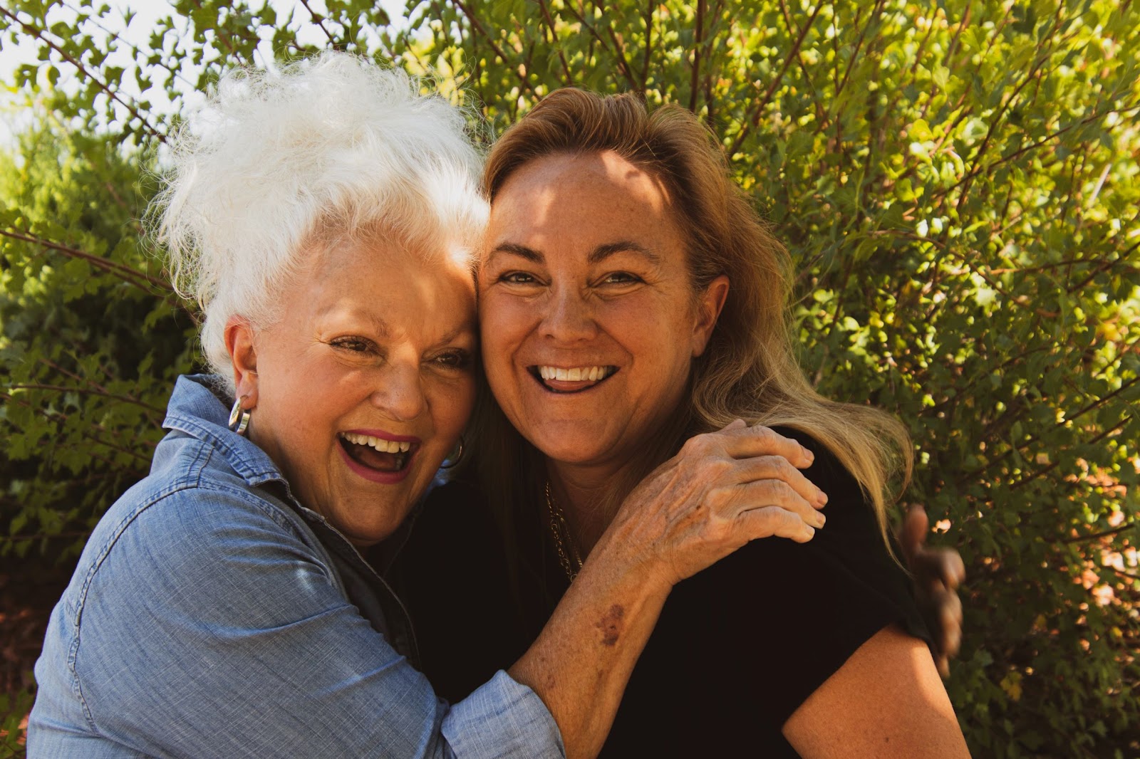 Two older woman hugging by a tree